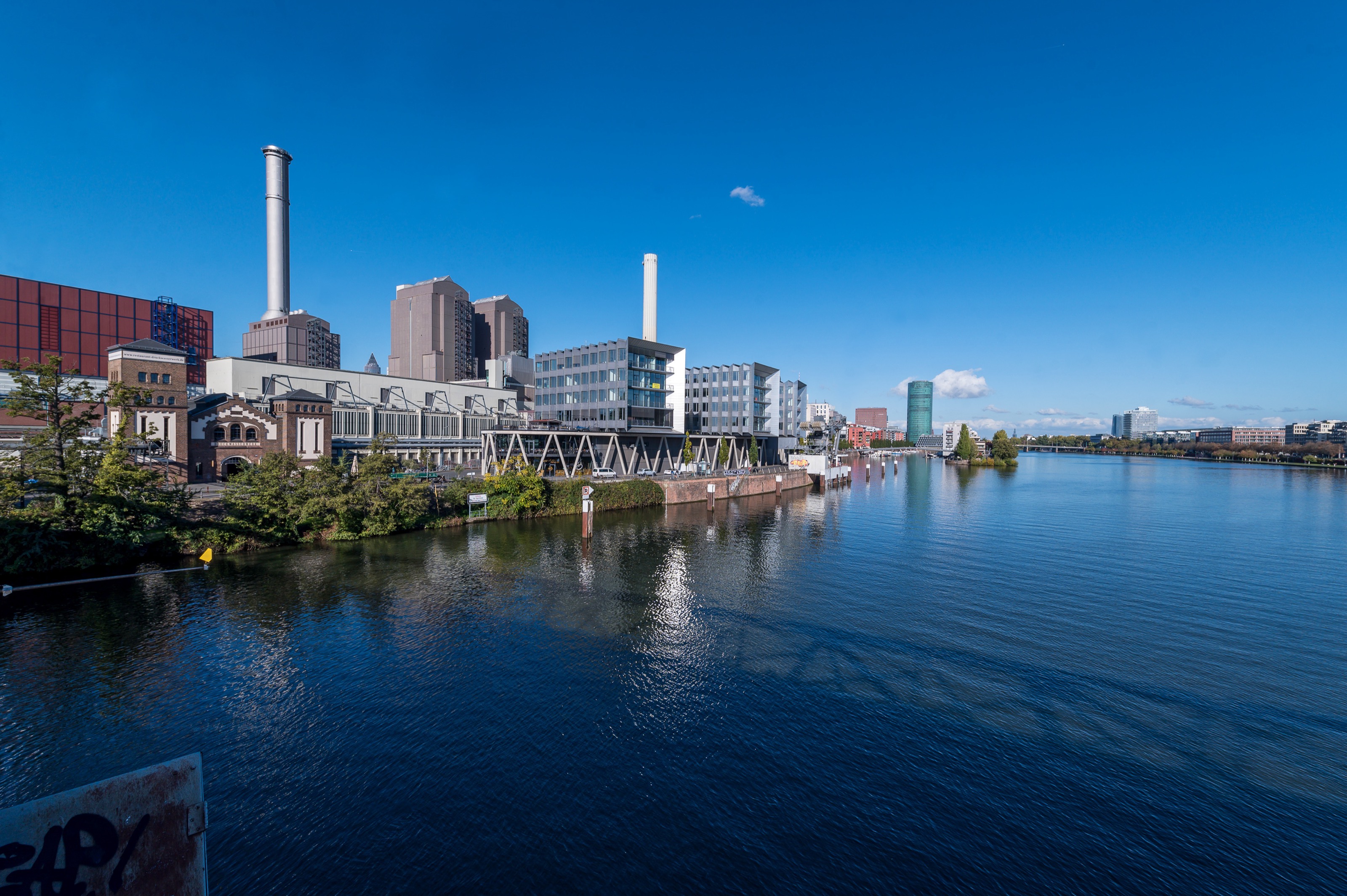 Von einer Brücke sieht man den Main und links davon den Westhafen Pier. Dahinter ist der Westhafen Tower, auch das „Gerippte“ genannt, zu erkennen.