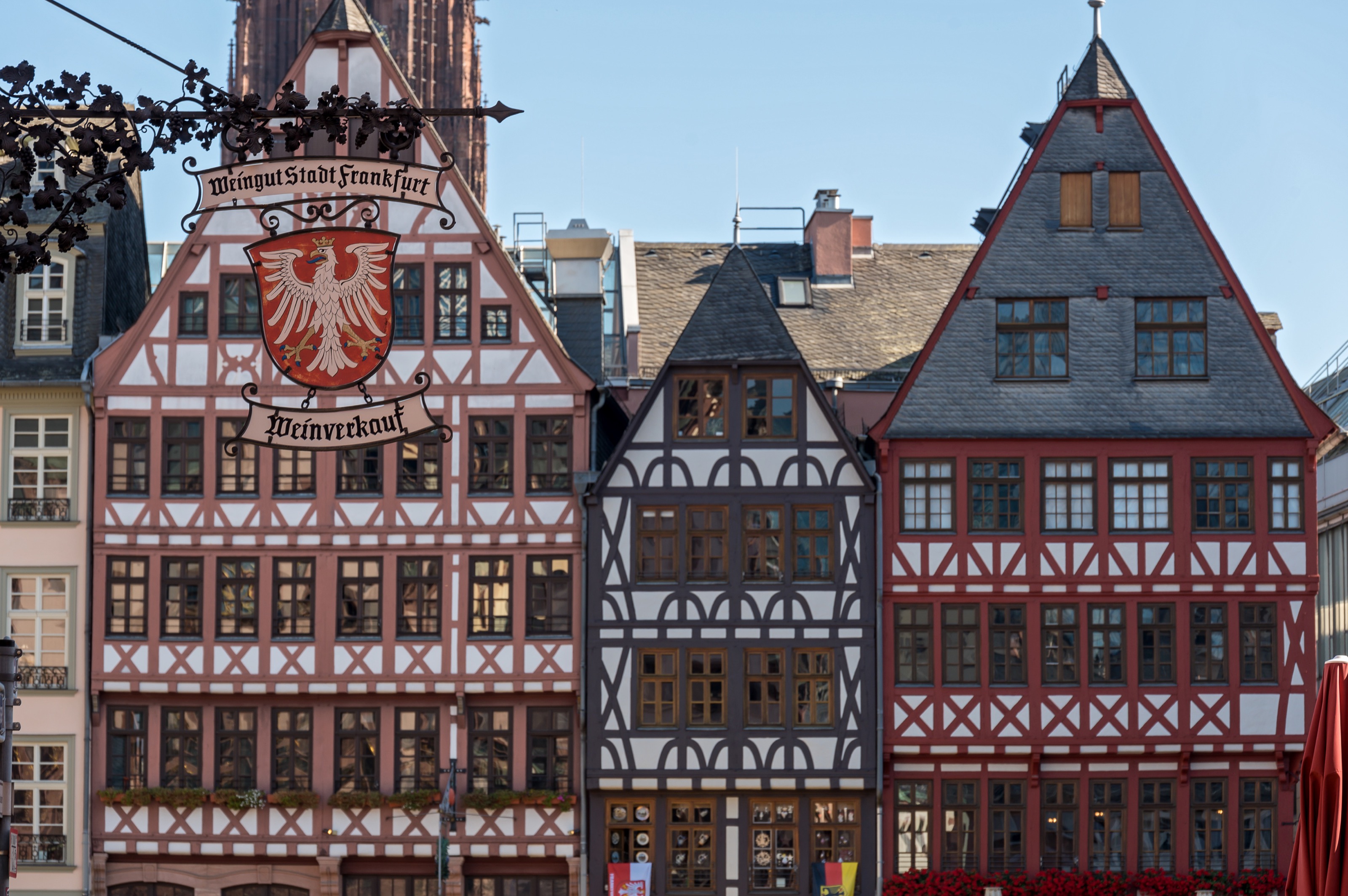 Im Vordergrund ragt von der linken Seite das Wappen des Frankfurter Weinguts ins Bild. Hierauf ist ein weißer Adler auf rotem Hintergrund zu sehen. Im Hintergrund des Wappens sind drei Fachwerkhäuser des Römerbergs zu erkennen.